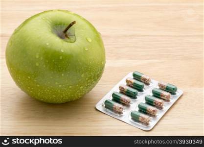 Green transparent pills capsules and fresh green apple. Green transparent pills capsules and fresh green apple on wooden background
