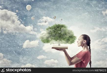 Green tree concept. Young woman in red dress holding opened book with green tree