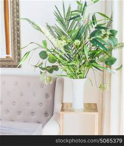 Green tropical houseplants bunch in vase near the couch in luxury living room. Home decoration and interior
