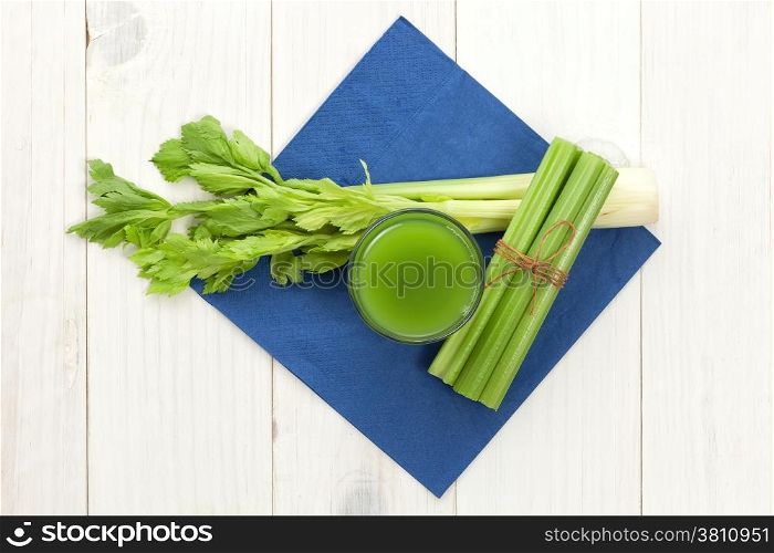 Green vegetable juice with celery on white wood background