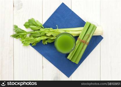Green vegetable juice with celery on white wood background