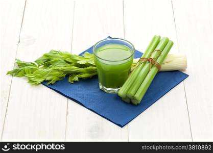 Green vegetable juice with celery stalk on white wood