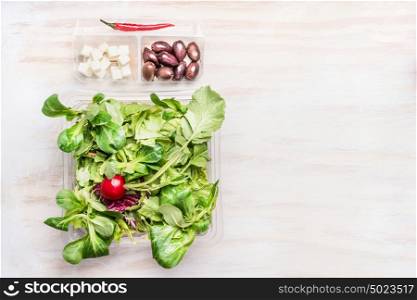 Green vegetable salad bowl with olives and feta cheese on white wooden background, top view, copy space. Healthy eating, dieting or vegetarian food concept