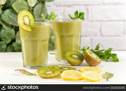 Green vegetable smoothie. Glasses of green vegetable smoothie. Green vegetable smoothie and ingredients: Kiwi, lemon and herbs.