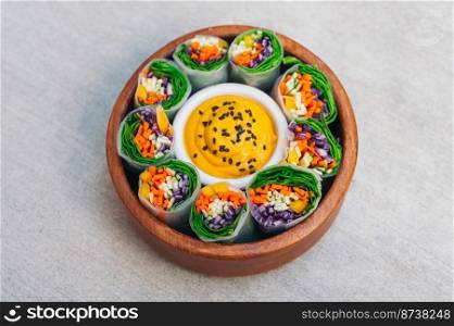 Green vegetarian spring rolls in bowl around curry sauce. Appetizing rolls filled with carrot, cucumber and purple cabbage, made of spinach.
