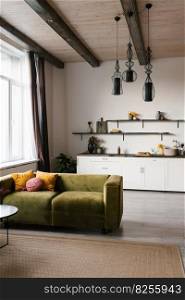 Green velour sofa with bright pillows in the Scandinavian living room with kitchen
