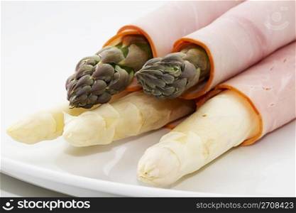 green white asparagus with ham. some green and white asparagus enrolled with ham on a white plate