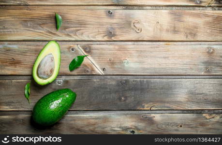 Green whole and cut avocado with leaves. On a brown wooden background.. Green whole and cut avocado with leaves.