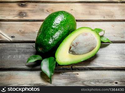 Green whole and cut avocado with leaves. On a brown wooden background.. Green whole and cut avocado with leaves.