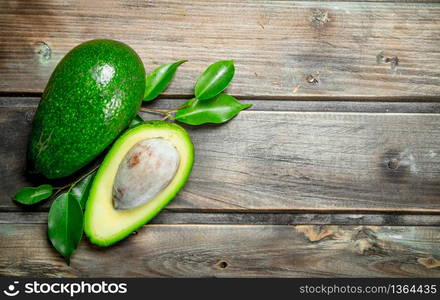 Green whole and cut avocado with leaves. On a brown wooden background.. Green whole and cut avocado with leaves.