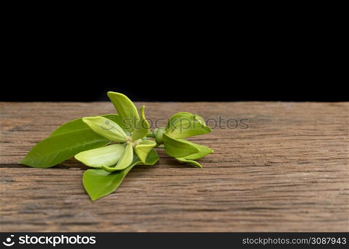 Green ylang-ylang flowers laid on an old wooden floor against a black background.