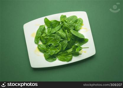 Green young spinach leaves in a white plate on a green table. Flat lay image with green raw food