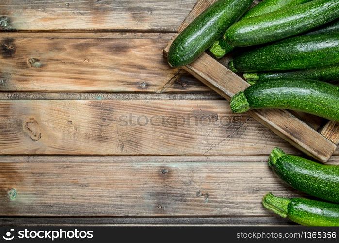 Green zucchini in wooden tray. On wooden background. Green zucchini in wooden tray.