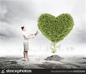 Greenery concept. Young attractive businesswoman cutting lawn in shape of heart