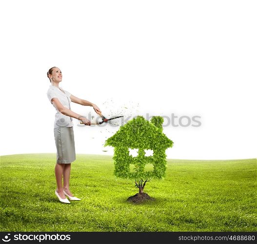 Greenery concept. Young attractive businesswoman cutting lawn in shape of house