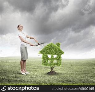 Greenery concept. Young attractive businesswoman cutting lawn in shape of house