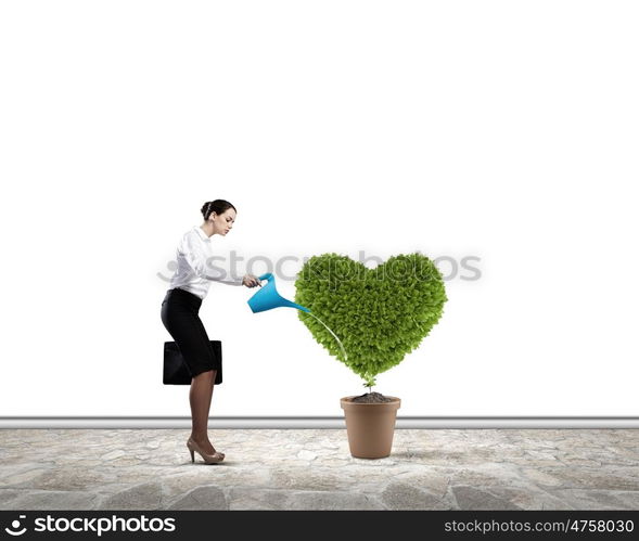 Greenery concept. Young attractive businesswoman watering plant in pot with can