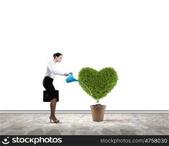 Greenery concept. Young attractive businesswoman watering plant in pot with can