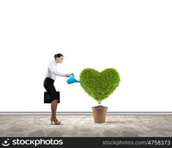 Greenery concept. Young attractive businesswoman watering plant in pot with can