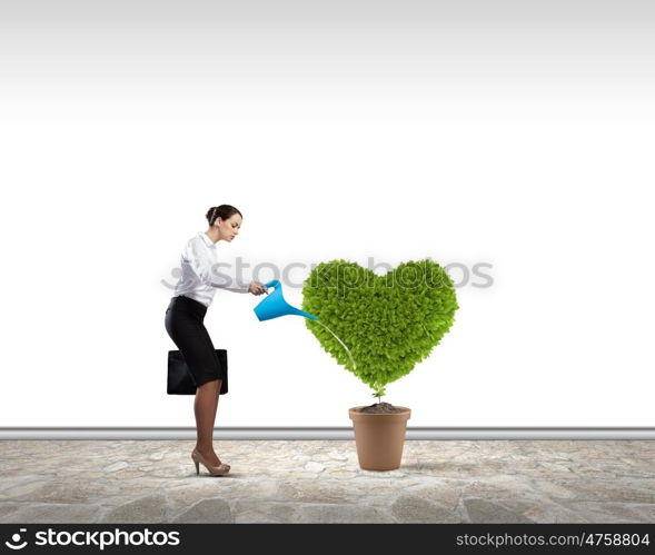 Greenery concept. Young attractive businesswoman watering plant in pot with can