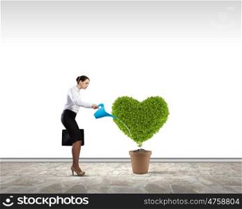 Greenery concept. Young attractive businesswoman watering plant in pot with can