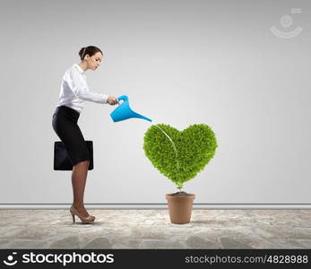 Greenery concept. Young attractive businesswoman watering plant in pot with can