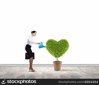 Greenery concept. Young attractive businesswoman watering plant in pot with can