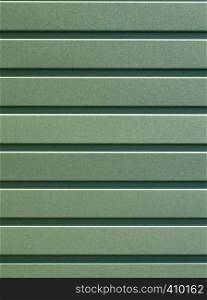 Greenery metallic fence made of corrugated steel sheet with vertical guides. Corrugated green iron sheet background close up.. Green corrugated steel sheet with vertical guides.