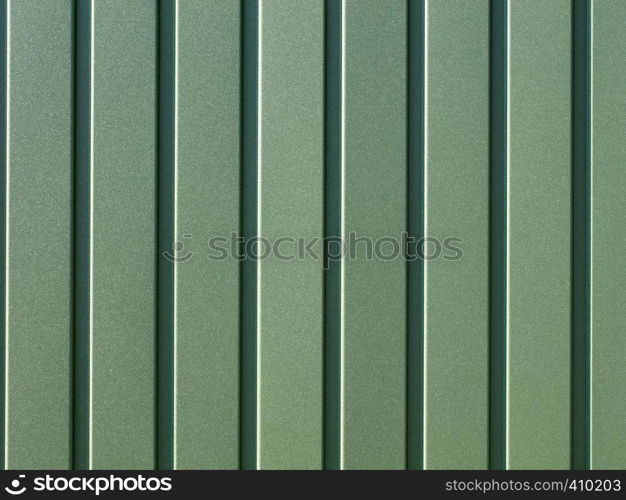 Greenery metallic fence made of corrugated steel sheet with vertical guides. Corrugated green iron sheet background close up.. Green corrugated steel sheet with vertical guides.