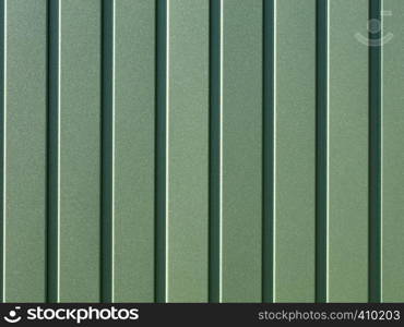 Greenery metallic fence made of corrugated steel sheet with vertical guides. Corrugated green iron sheet background close up.. Green corrugated steel sheet with vertical guides.