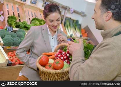 Greengrocer holding basket of produce for customer