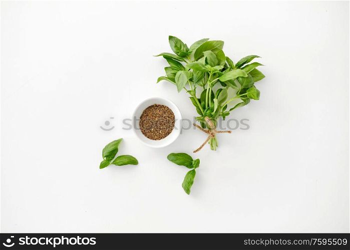 greens, culinary and flavoring concept - bunch of fresh basil herb and dry seasoning in cup on white background. fresh basil and dry seasoning on white background