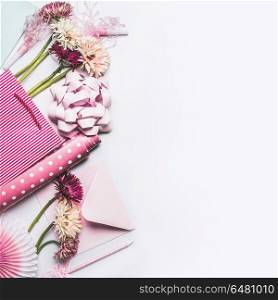 Greeting accessories setting with flowers, bow, ribbon, pink gift wrapping paper and shopping bag on white desktop background, Top view , copy space, flat lay