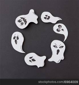 Greeting card, creative application with handmade paper terrible spirits smiling and laughing ghosts on a black background, copy space. Flat lay. Happy Halloween. Handcraft round frame of flying floating singing smiling specters on a black background.