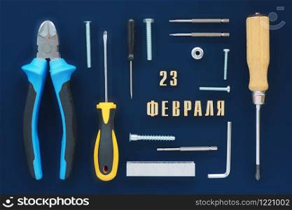 Greeting card. male tools, wire cutters, screwdrivers, wrenches, bolts, staples for a stapler, screws, nuts, and an inscription in Russian from February 23 on a dark blue background.