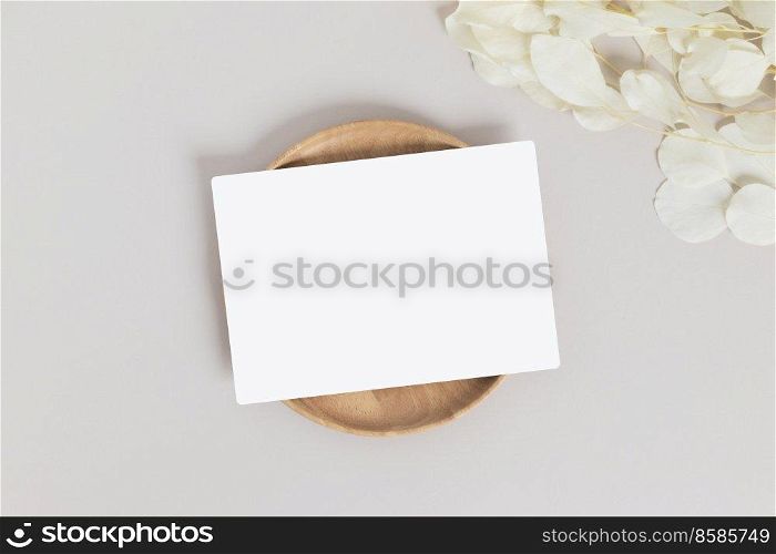 Greeting card or invitation card with white dry flower leaves on wood plate or tray in beige background
