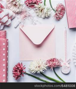 Greeting flat lay with pastel pink envelope, pen, flowers, ribbon and accessories on white desk , top view, flat lay