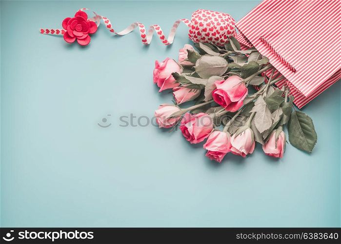 Greeting pink pale roses bunch in shopping bag with ribbon on turquoise blue background, top view, copy space. Female holidays layout.