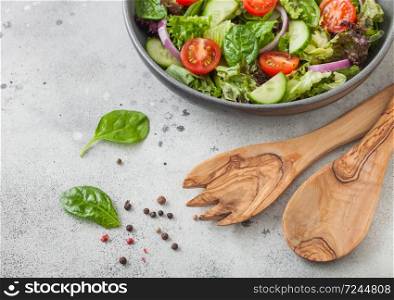 Grey bowl with healthy fresh vegetables salad with lettuce and tomatoes, red onion and spinach on light table background with spatula spoon and fork. Top view