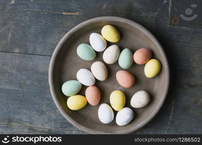 Grey Ceramic Plate with painted Easter Eggs of pastel colors on vintage wooden background. Happy Easter card concept, minimalistic design, top view