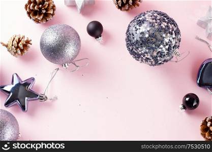 Grey Christmas decorations and cones border on pink background, top view frame. Gray Christmas decorations on pink