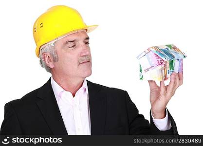 Grey-haired architect holding house made from bank notes