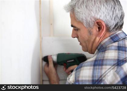 Grey haired handyman drilling into wall