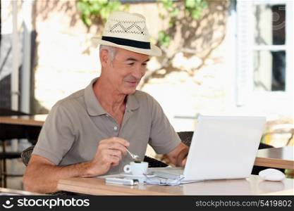 Grey haired man drinking coffee on terrace with laptop computer