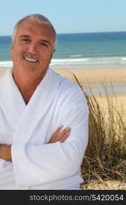 Grey haired man in bathing robe stood on beach