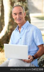 Grey haired man in park with laptop computer