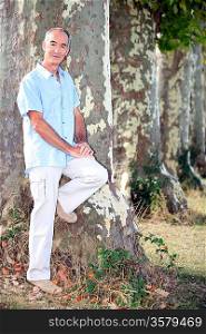 Grey-haired man leaning against tree