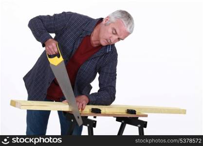 Grey-haired man sawing plank of wood