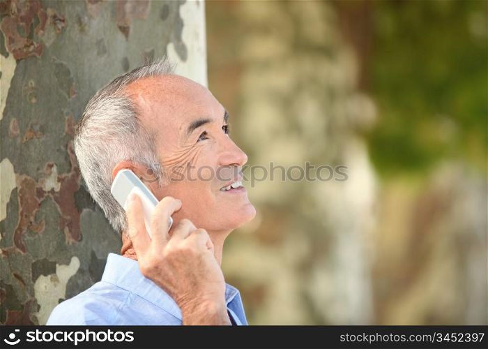 Grey-haired man with mobile telephone stood by tree