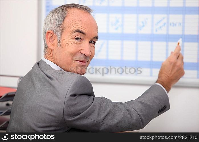 Grey haired man writing on calendar
